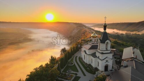 Aerial drone cinematic view of sunrise morning at Orheiul Vechi monastery with red sky and misty fog, dramatic epic shot - Starpik Stock
