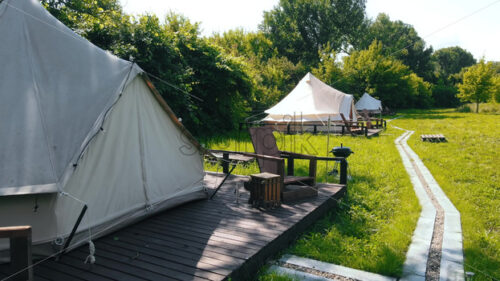 Glamping cinematic tents with chairs in the nature, green grass and trees, trail - Starpik Stock