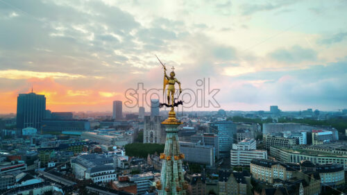 Aerial drone cinematic view of statue of Saint Michael atop the spire of the Brussels Town Hall at sunset in Belgium. Multiple buildings on the background - Starpik Stock