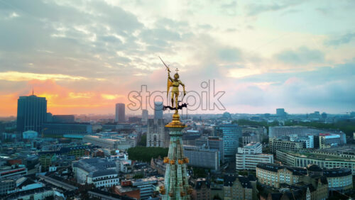 Video - Aerial drone cinematic view of statue of Saint Michael atop the spire of the Brussels Town Hall at sunset in Belgium. Multiple buildings on the background