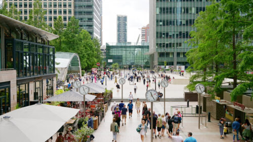 Video – LONDON, UNITED KINGDOM – SEPTEMBER 12, 2023: cinematic Street scape of the Canary Wharf district with Six Public Clocks square full of people and greenery, skyscrapers around - Starpik Stock