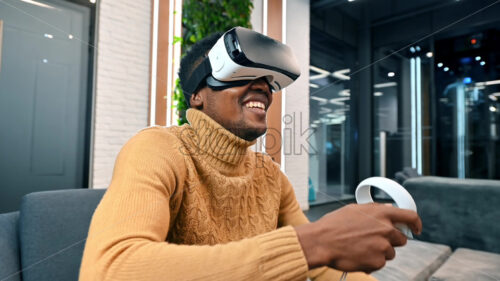 A black man exploring virtual reality using VR glasses and controllers in an office - Starpik