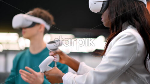 A black woman exploring virtual reality using VR glasses in an office, other people in VR glasses nearby, virtual reality - Starpik Stock