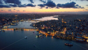 Aerial drone view of Istanbul at sunset, Turkey. Multiple residential buildings, mosques, Galata and Metro bridges over the Golden Horn waterway with multiple floating ships, nightlights - Starpik