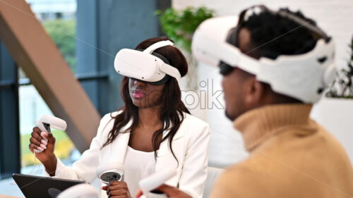 Business conference in VR in an office. A black man and woman using VR glasses and controllers, virtual reality - Starpik Stock