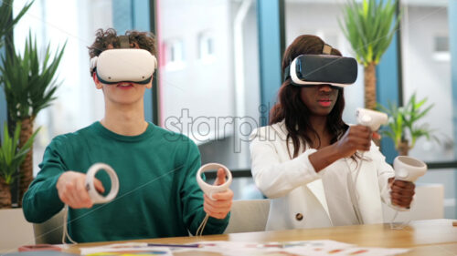 Business conference in VR in an office. Multiracial group of people talking and using VR glasses and controllers, papers on the table, virtual reality - Starpik Stock