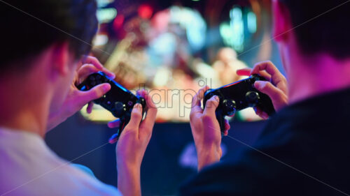 Chisinau, Moldova – September 9, 2023: Two teen friends are playing a game console using gamepads, close view of hands, TV on the background. Blue and red illumination - Starpik Stock