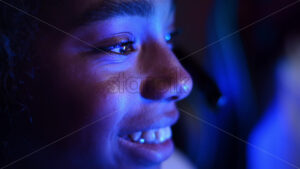 Close view of a black teen smiling girl playing video games in video game club with blue illumination. Slow motion - Starpik