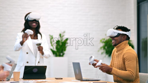 Female team leader at business conference in VR in an office. Multiracial group of people using VR glasses and controllers, papers and gadgets on the table, virtual reality - Starpik Stock