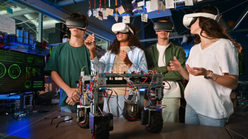 Group of young people in VR glasses discussing and doing experiments in robotics in a laboratory. Robot on the table - Starpik