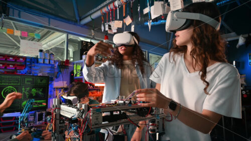 Group of young people in VR glasses doing experiments in robotics in a laboratory. Gesticulating. Robots on the table - Starpik