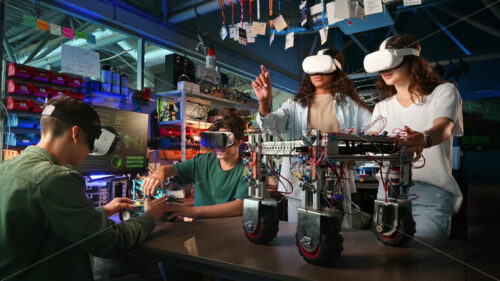 Group of young people in VR glasses doing experiments in robotics in a laboratory. Robots on the table - Starpik