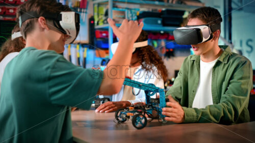 Group of young people in VR glasses doing experiments in robotics in a laboratory. Robots on the table, virtual reality - Starpik Stock