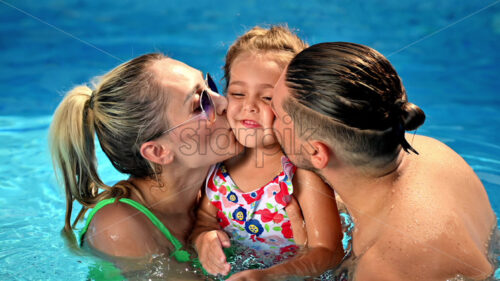 Happy parents kissing their smiling daughter while swimming in the pool. Slow motion - Starpik