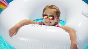 Little girl in sunglasses resting on white pool balloon - Starpik