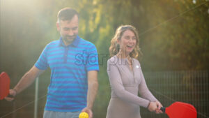 Man and woman playing pickleball in a team. Greenery on background. Outdoor court. Slow motion - Starpik