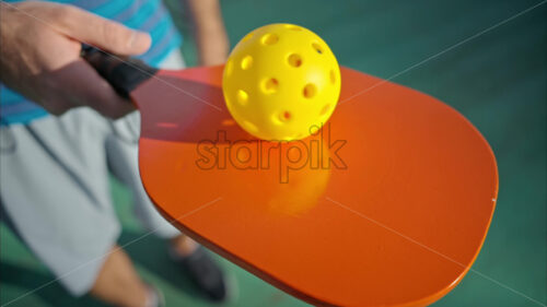 Man spinning pickleball ball on orange paddle. Sunny outdoor - Starpik