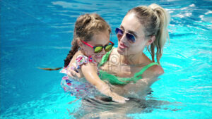 Mother and daughter resting and swimming in a pool in summer - Starpik