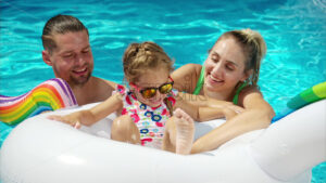 Mother with father and daughter smiling and resting and swimming in a pool in summer, white pool balloon - Starpik