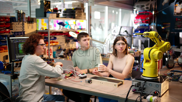 Premium stock video footage – Young happy engineers programming an yellow robotic arm in the workshop to grab cardboard water glass, computer programming training for coffee preparation, celebrating success - Starpik Stock