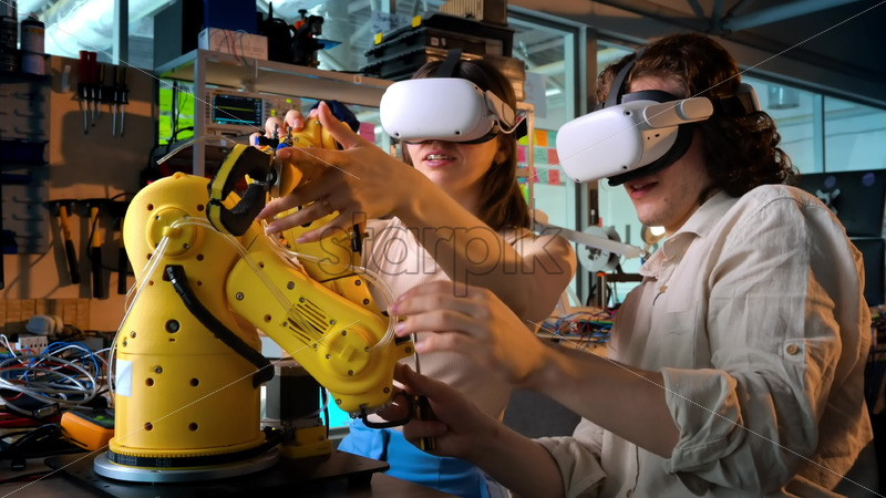 Video - Premium stock video footage - Young man and woman in VR glasses doing experiments in robotics in a laboratory. Robot and tools on the table. Slow motion, virtual reality