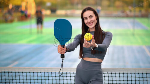 Smiling woman in sports suit posing with ball and racket for playing Pickleball on an outdoor court. Slow motion - Starpik