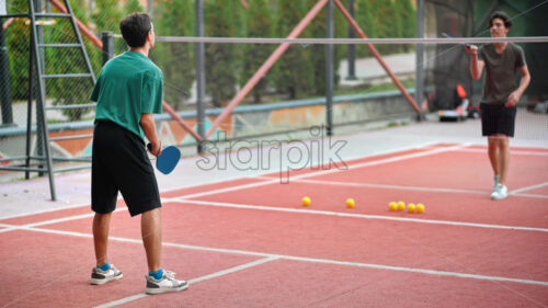 Two young guys playing Pickleball, hitting the ball with a racket on an outdoor court. Slow motion - Starpik