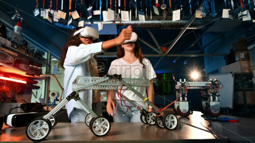 Two young women in VR glasses doing experiments in robotics in a laboratory. Gesticulating. Robots on the table - Starpik