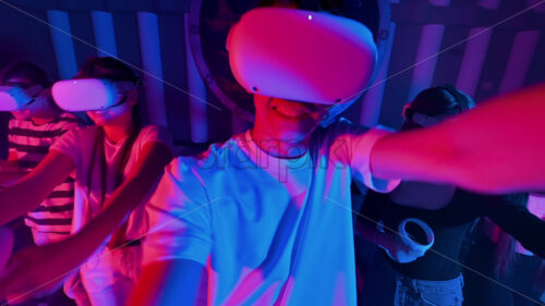 Video – A team of young friends play virtual reality games in VR equipment on an arena. Neon lights - Starpik Stock