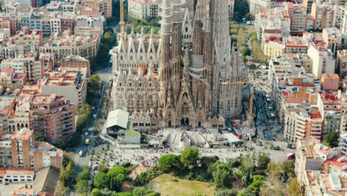 Video - Aerial drone view of Sagrada Familia in city downtown. People and residential districts around, greenery
