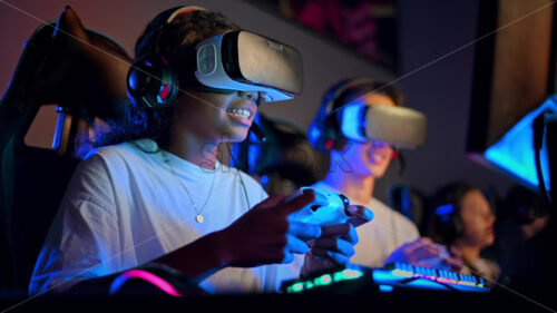 Video – Premium stock video footage – White boy and black girl teens in VR headsets playing video games in video game club with blue illumination using a gamepad, virtual reality - Starpik Stock