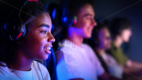 Video – Premium stock video footage – White boy and black girl teens in headsets playing video games in video game club with blue and red illumination. Slow motion - Starpik Stock