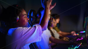 White boy and black girl teens in headsets playing video games in video game club with blue and red illumination, giving each other five - Starpik