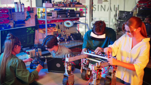 Young engineers with VR virtual reality headset fixing a robotic car in research laboratory, slow motion - Starpik