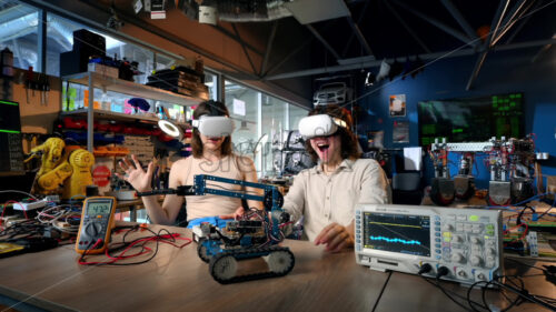 Young man and woman in VR glasses doing experiments in robotics in a laboratory. Giving each other five. Robot and tools on the table. Slow motion, virtual reality - Starpik Stock