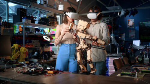 Young man and woman in VR glasses doing experiments in robotics in a laboratory. Robot and tools on the table. Slow motion, virtual reality - Starpik Stock