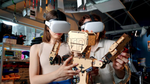 Young man and woman in VR glasses doing experiments in robotics in a laboratory. Robot on the table. Slow motion - Starpik