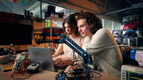 Young man and woman in protective glasses doing experiments with electricity in a laboratory. Tools on the table - Starpik