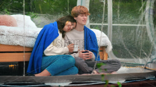 A couple hugging each other and talking on a tent terrace at glamping. Lush forest around - Starpik Stock