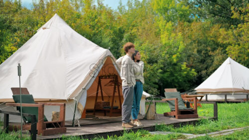 A couple hugging each other and talking on a tent terrace at glamping. Lush forest around - Starpik Stock