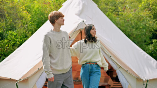 A couple hugging each other and talking on a terrace at glamping, view from inside a tent. Lush forest around - Starpik Stock