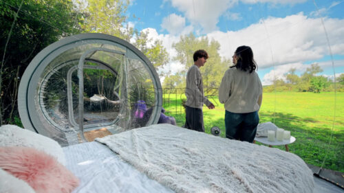 A couple hugging each other inside a bubble tent at glamping. Lush forest around - Starpik Stock