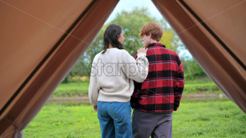 A couple sitting under a blanket on a tent terrace, holding cups and talking at glamping. Lush forest around - Starpik Stock