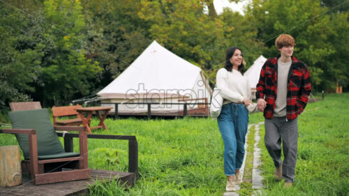 A couple talking and walking along tents at glamping. Lush forest around - Starpik Stock