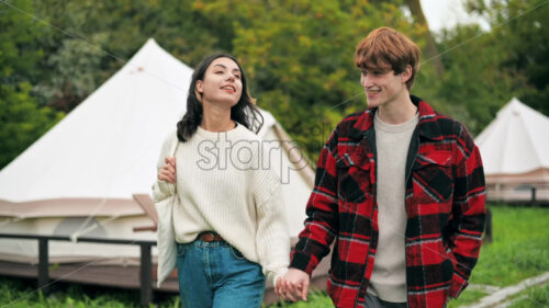 A couple talking and walking by the hand along tents at glamping. Lush forest around - Starpik Stock