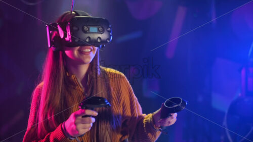 A joyful, interested girl is playing on VR treadmill with helmet and controllers. Slow motion virtual reality - Starpik Stock