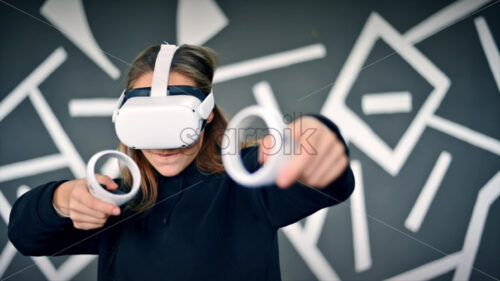 A young interested woman playing in VR games using VR glasses and controllers. Slow motion virtual reality - Starpik Stock