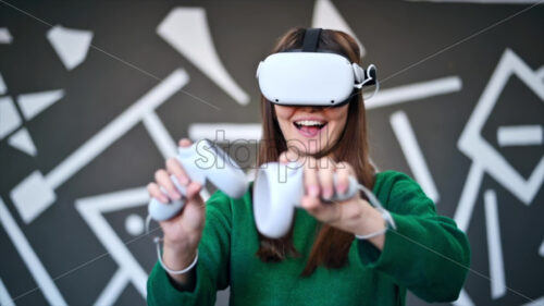 A young interested woman playing in VR games using VR glasses and controllers. Slow motion virtual reality - Starpik Stock