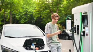 A young man using smartphone at a car charging station with charging electric car nearby. Chisinau, Moldova. Slow motion - Starpik Stock