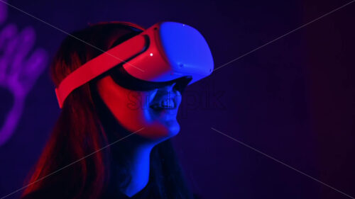 A young woman in VR glasses is smiling while playing VR games. Red and blue illumination. Slow motion virtual reality - Starpik Stock